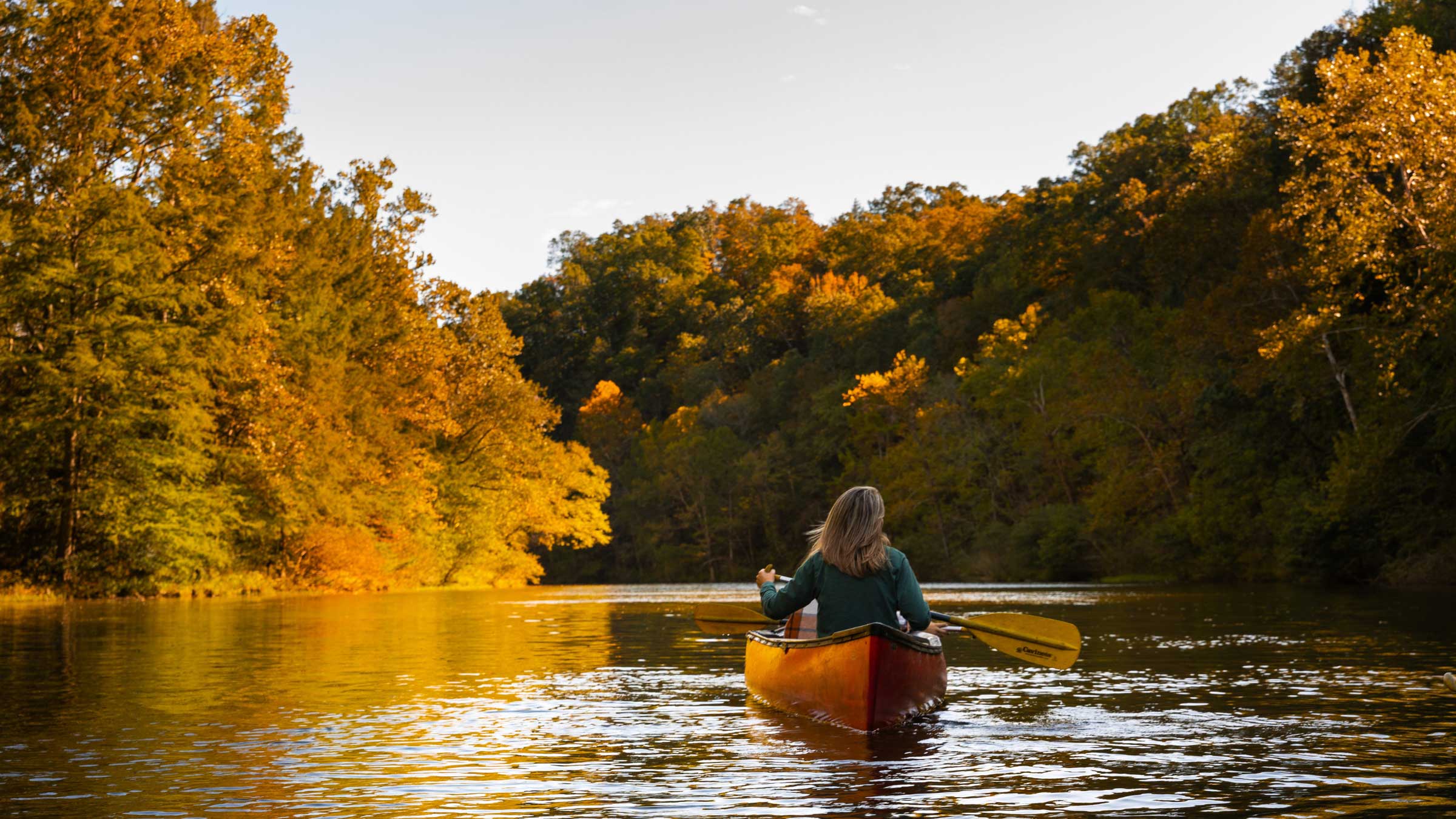 A woman kayaks alone in Beavers Bend State Park during the autumn fall season