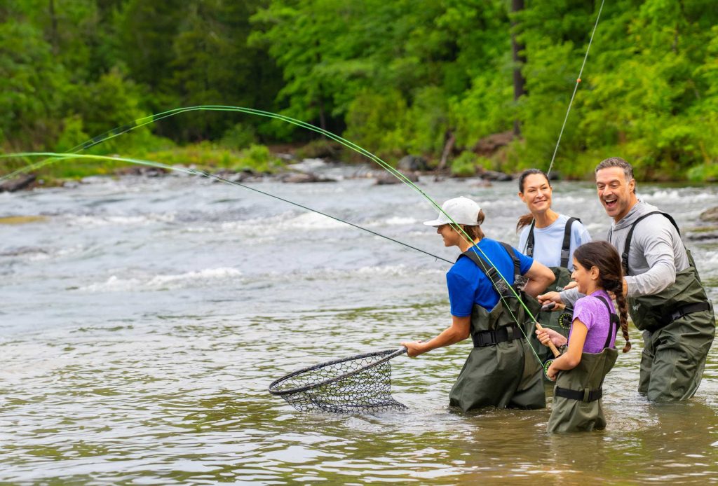 A fishing guide shows a family how to fly fish for rainbow trout on the Lower Mountain Fork River in Beavers Bend Cabin Country
