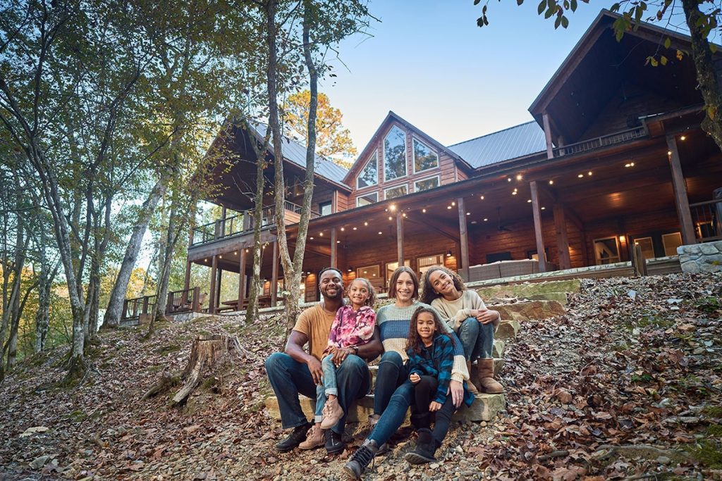 A young family sitting outside of a large log cabin in Beavers Bend Cabin Country, Southeastern Oklahoma