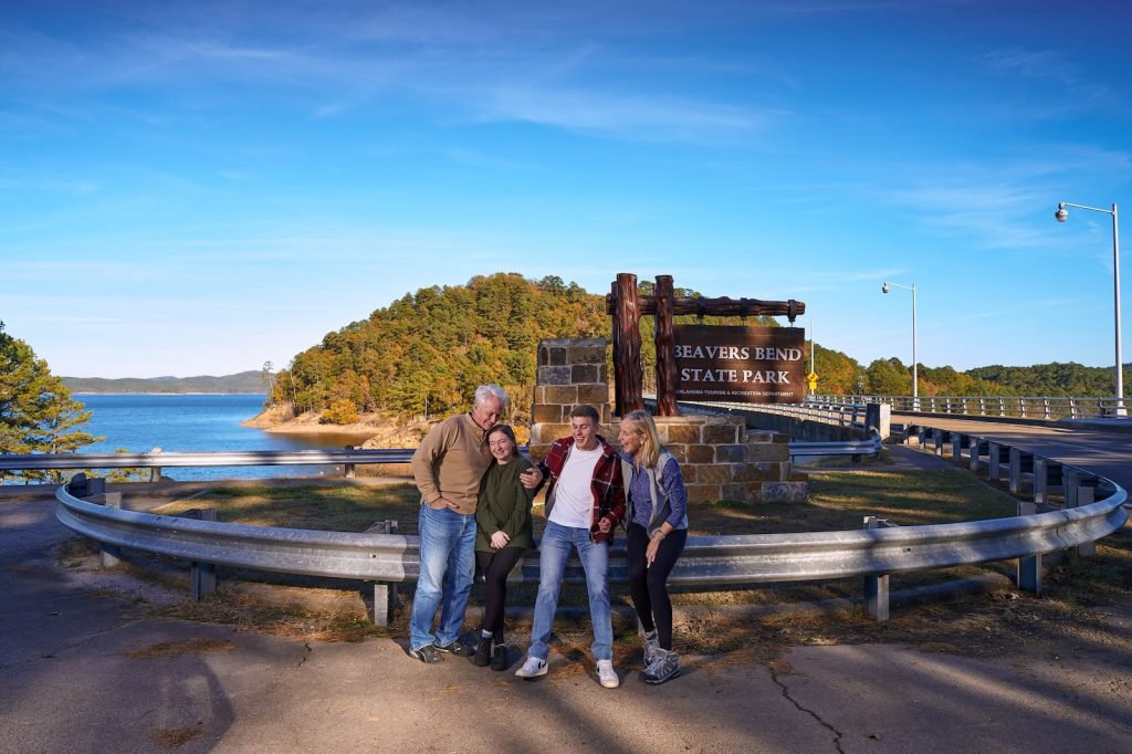 An older family posing next to the Beavers Bend State Park sign