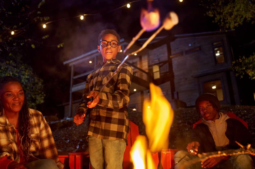 A boy in flannel roast marshmallows for s'mores over the campfire at their big cabin in Beavers Bend Cabin Country