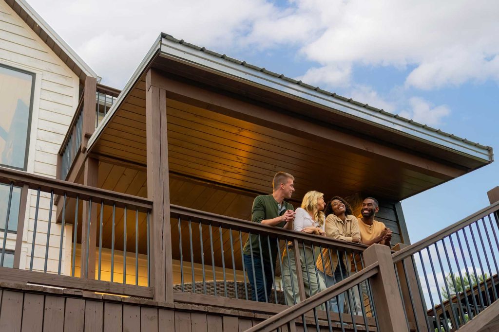 A friends group relaxes on the balcony of their luxury cabin rental in Beavers Bend Cabin Country.